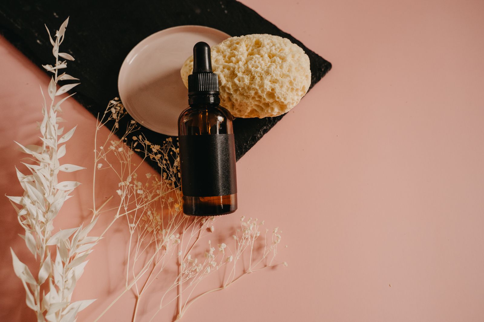 Flacon de sérum en verre ambré posé sur un fond rose