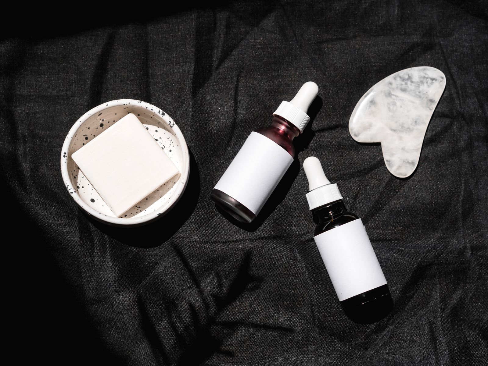Flacons de soin et gua sha disposés sur un fond sombre