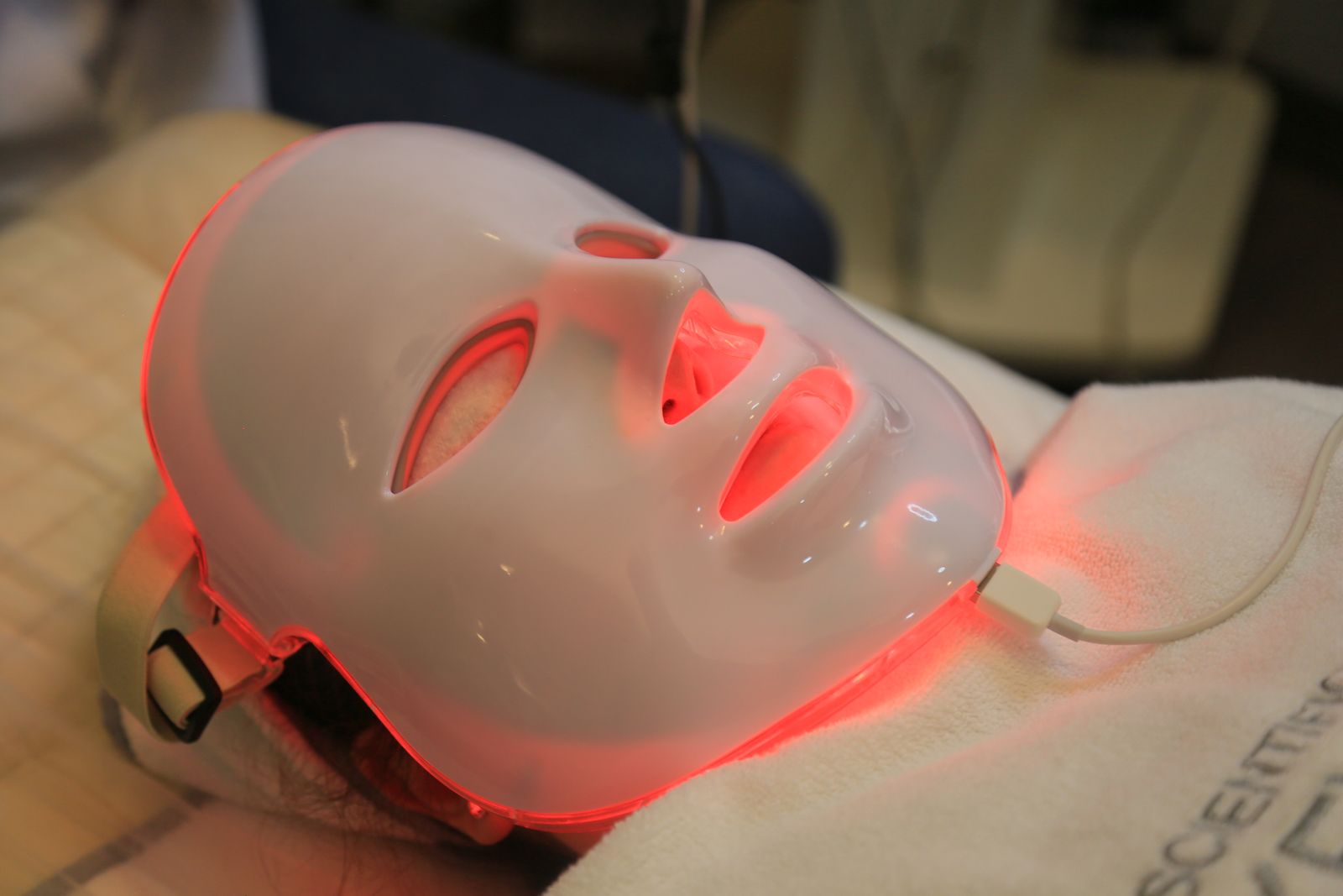 Masque LED de soin allumé en lumière rouge, posé sur une table de soin